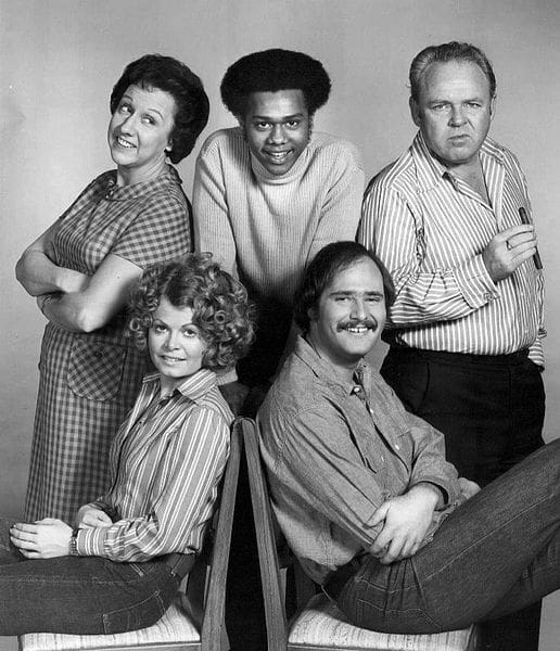 Photo of the cast of the television program All In the Family. Standing, from left: Jean Stapleton (Edith Bunker), Mike Evans (Lionel Jefferson), Carroll O'Connor (Archie Bunker). Seated: Sally Struthers (Gloria Bunker Stivic) and Rob Reiner (Mike Stivic).